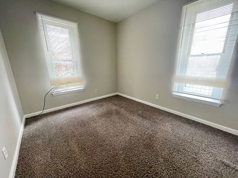 an empty bedroom with two windows and a carpeted floor