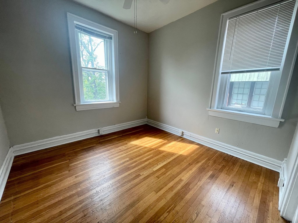 an empty bedroom with wood floors and two windows