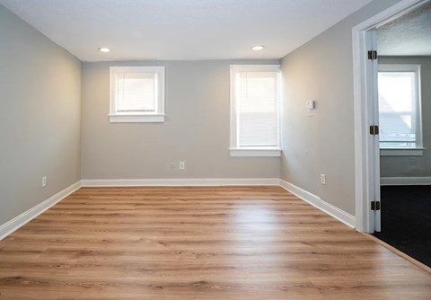 A room with wooden flooring and two windows.