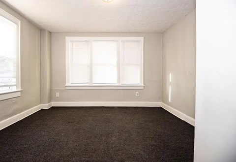 A room with a carpeted floor and a window with blinds.