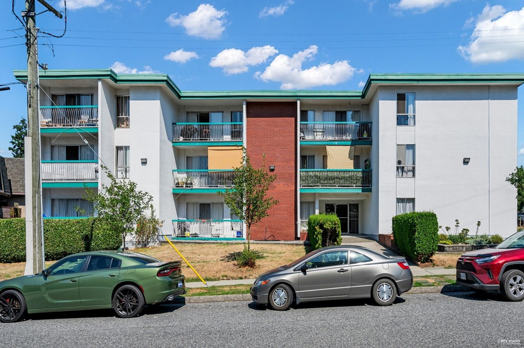 A green car is parked in front of a multi-story apartment building.