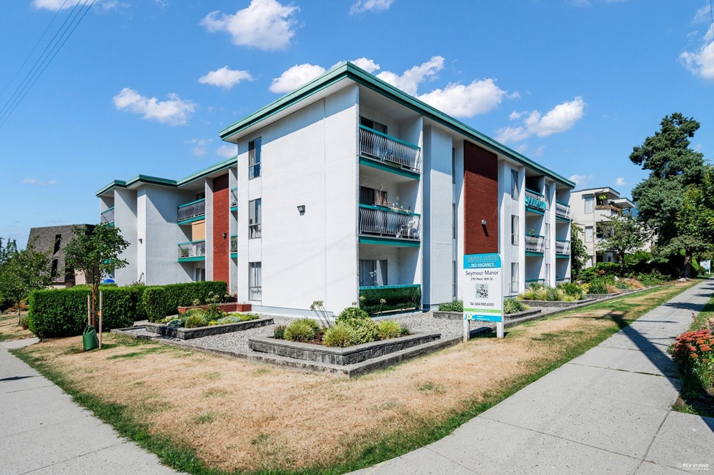 A white apartment building with a green roof and a sign in front.