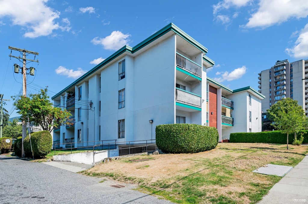 A white building with a green roof is surrounded by a grassy area and a sidewalk.
