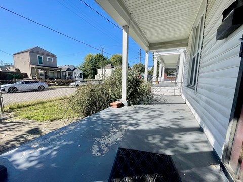 A white house with a porch and a car parked in the driveway.