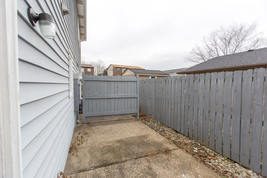 the back yard of a white house with a fence and a sidewalk