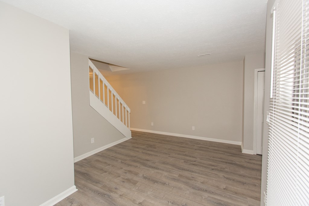 an empty living room with wood floors and a white staircase