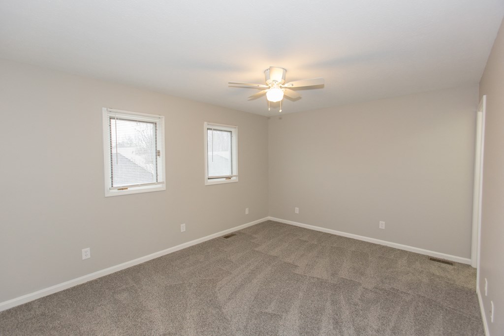 an empty living room with a ceiling fan and two windows