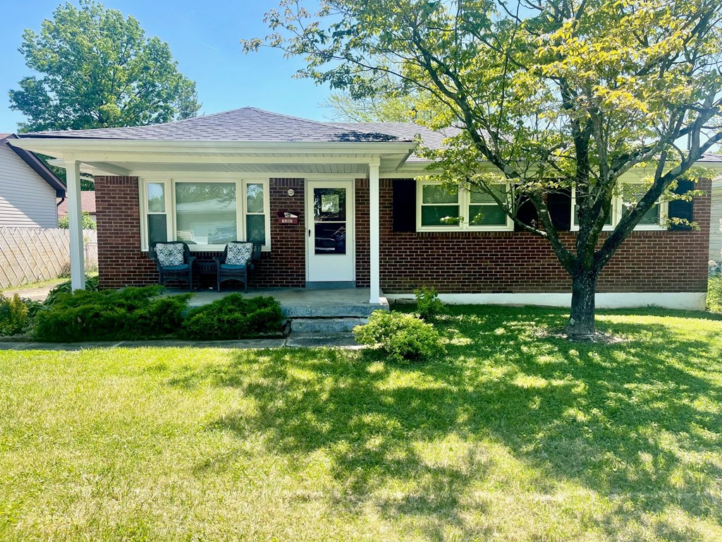 a small brick house with a porch and a tree