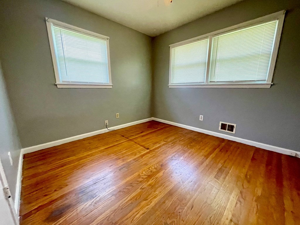 an empty room with wooden floors and two windows
