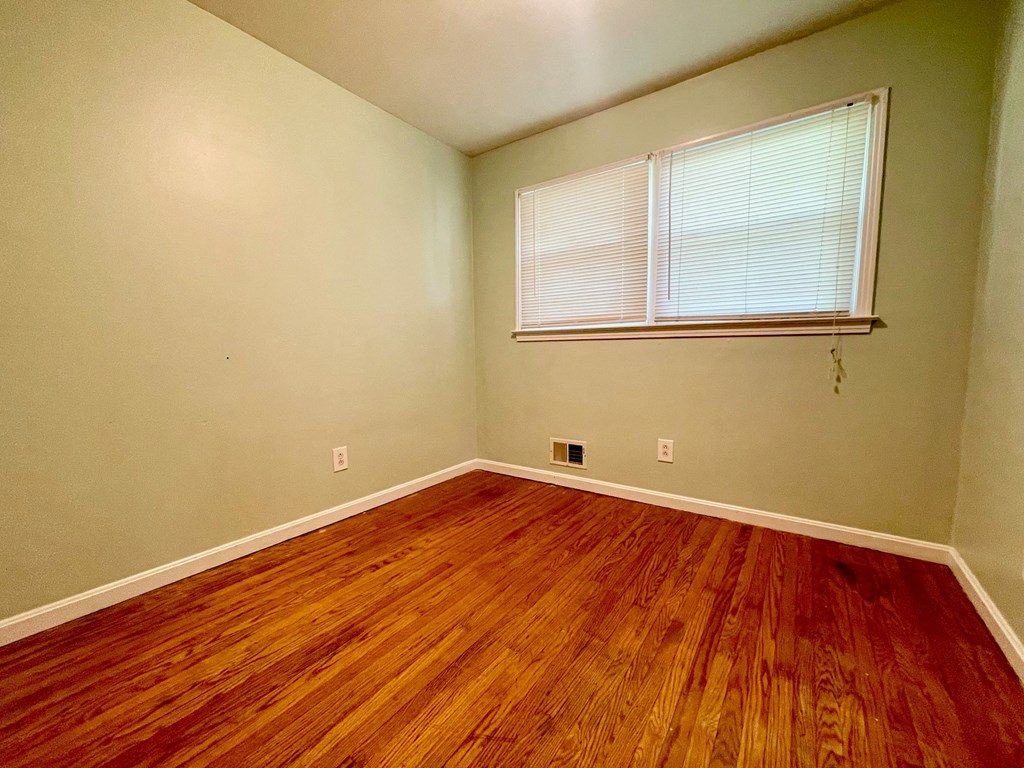 an empty bedroom with wood floors and a window