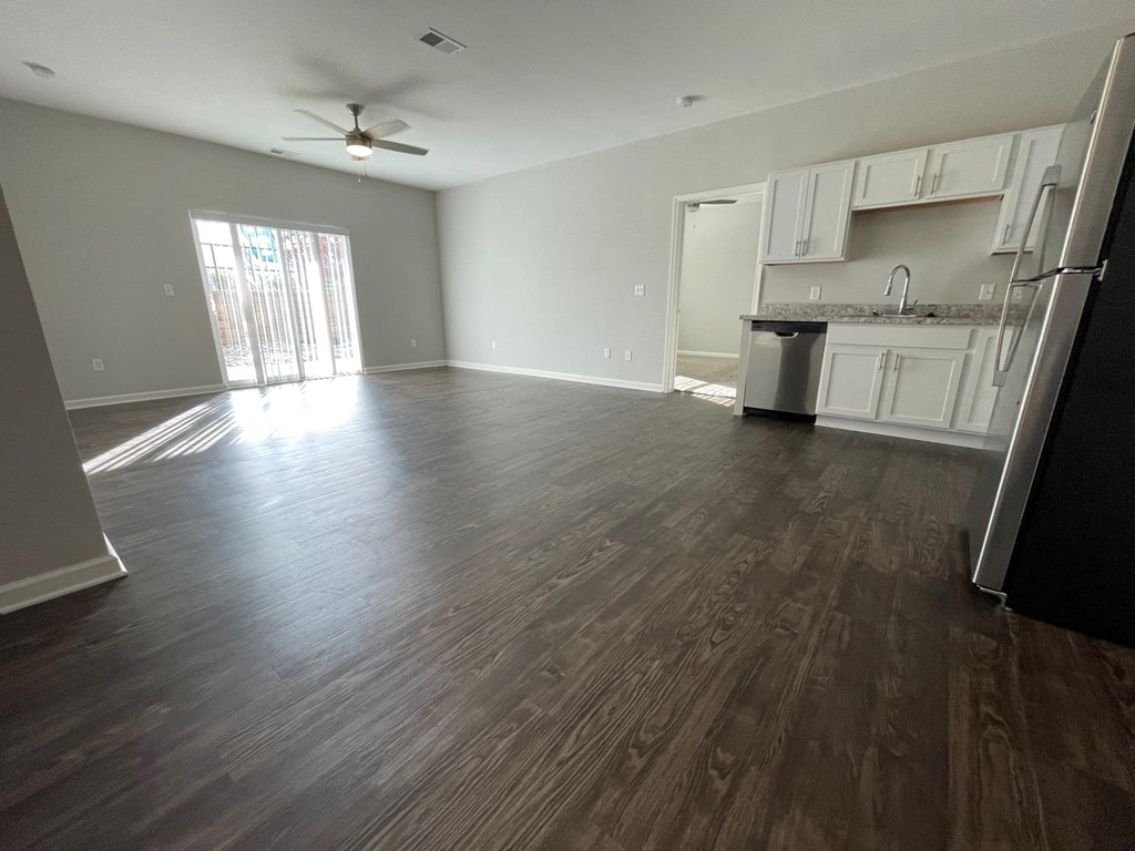 an empty living room with wood floors and a kitchen
