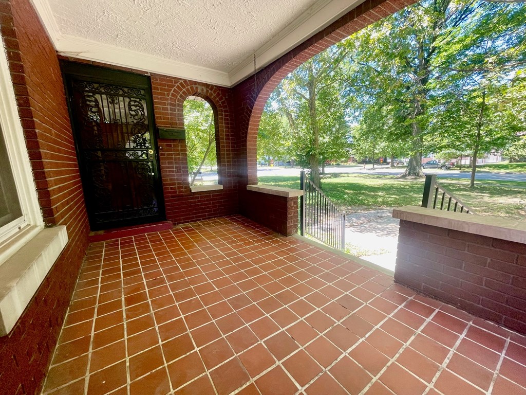 a covered porch with a view of a park and trees