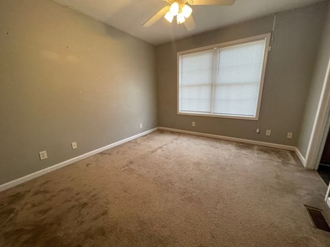 A room with a carpeted floor and a window with blinds.