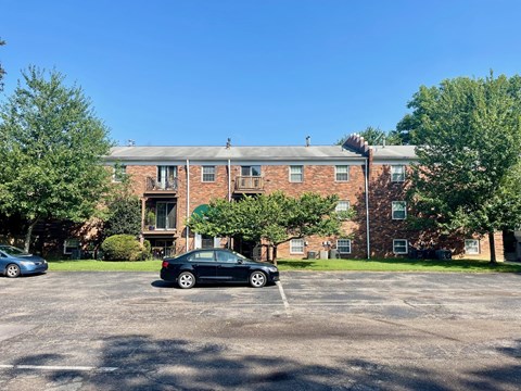 A black car is parked in a parking lot in front of a brick building.