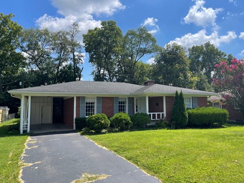 a small brick house with a driveway and a lawn