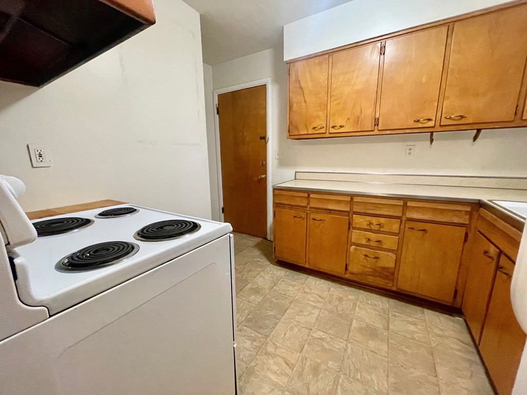 A kitchen with a white stove top oven and wooden cabinets.