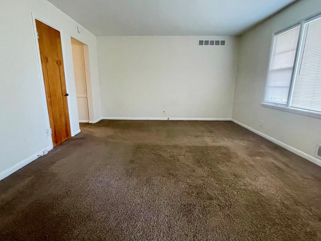 A room with brown carpet and a wooden door.