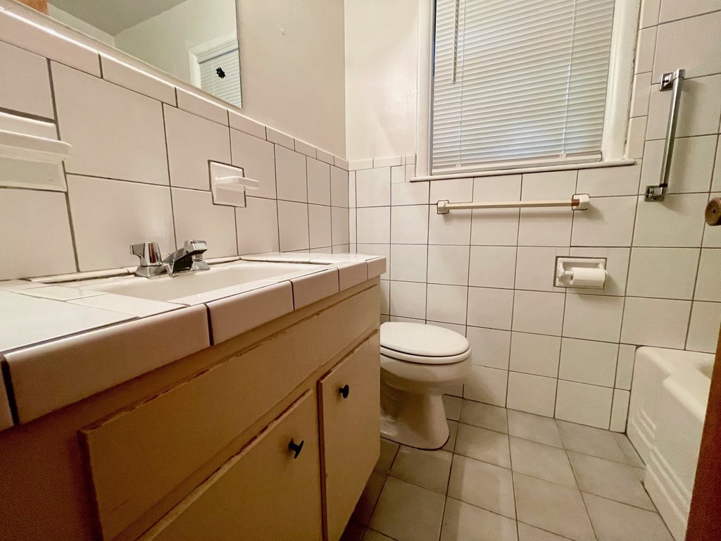 A white toilet sits in a bathroom with a white sink and wooden cabinets.