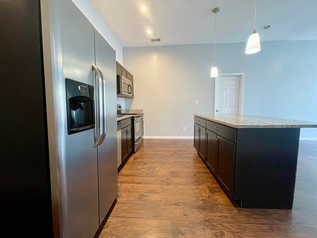 A kitchen with a stainless steel refrigerator and wooden flooring.