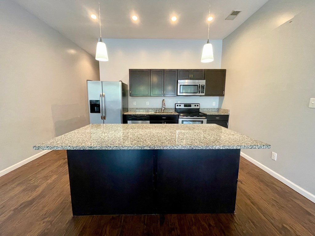 A kitchen with a granite countertop and dark wood cabinets.