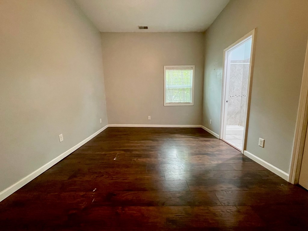 A room with a brown wooden floor and a window with blinds.