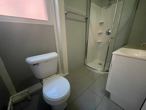 A white toilet sits in a small bathroom next to a walk-in shower.