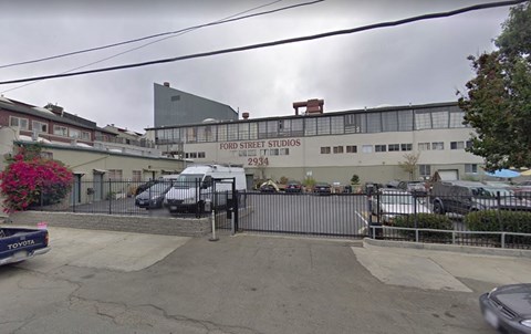The image shows a street view of Ford Street Studios with a grey building and a black van parked in front.