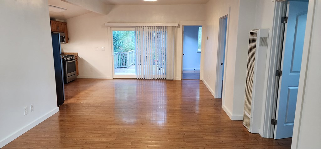 an empty living room with wood floors and a door to a balcony