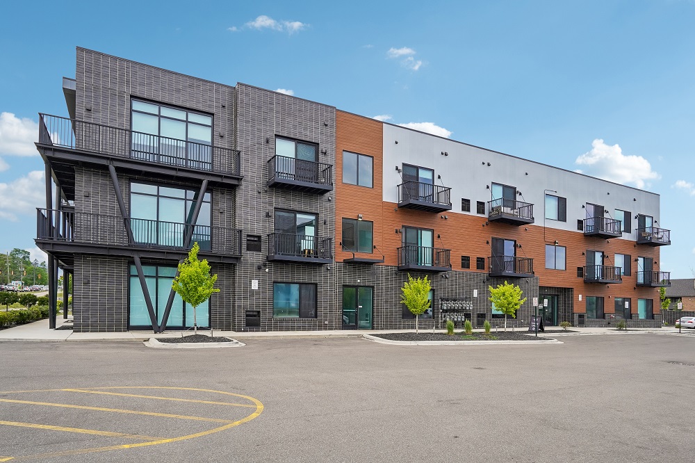 A modern multi-story building with balconies and a parking lot in front.