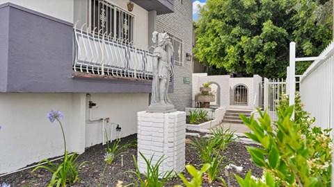 A white statue of a woman stands in front of a house.