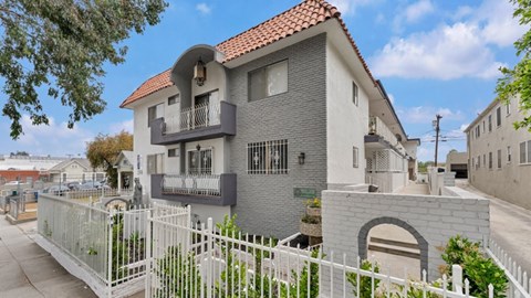 A grey house with a red roof and a white fence in front.