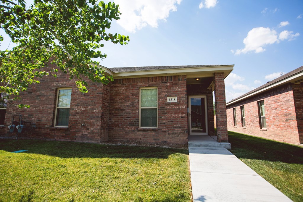 the front of a brick building with a sidewalk and grass