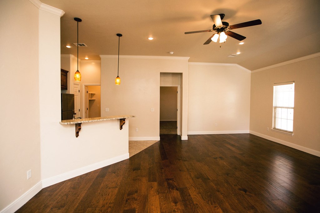 an empty living room with a ceiling fan and a kitchen