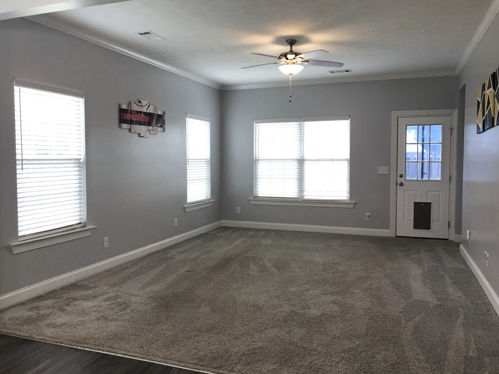 an empty living room with a ceiling fan and windows
