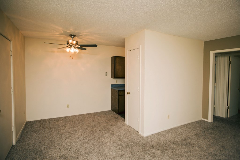 an empty living room with a ceiling fan and a door to a kitchen