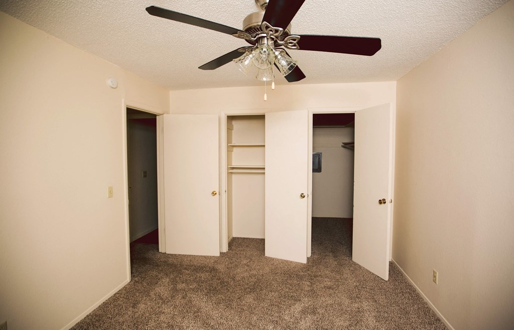 an empty bedroom with a ceiling fan and closet