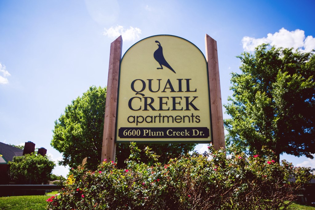 a sign for quail creek apartments in front of trees