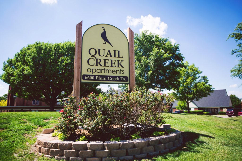 a sign for quail creek apartments in front of a grass field