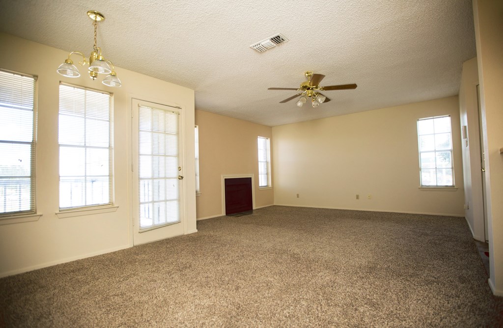 an empty living room with a ceiling fan and windows