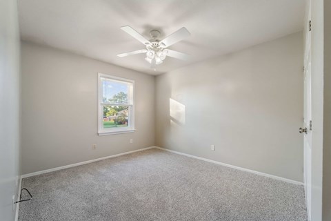 A room with a ceiling fan and a window showing a view of trees.