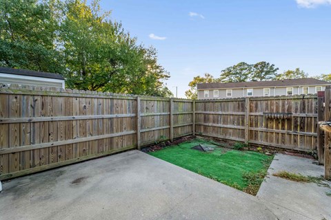 A backyard with a wooden fence and a green patch of grass.