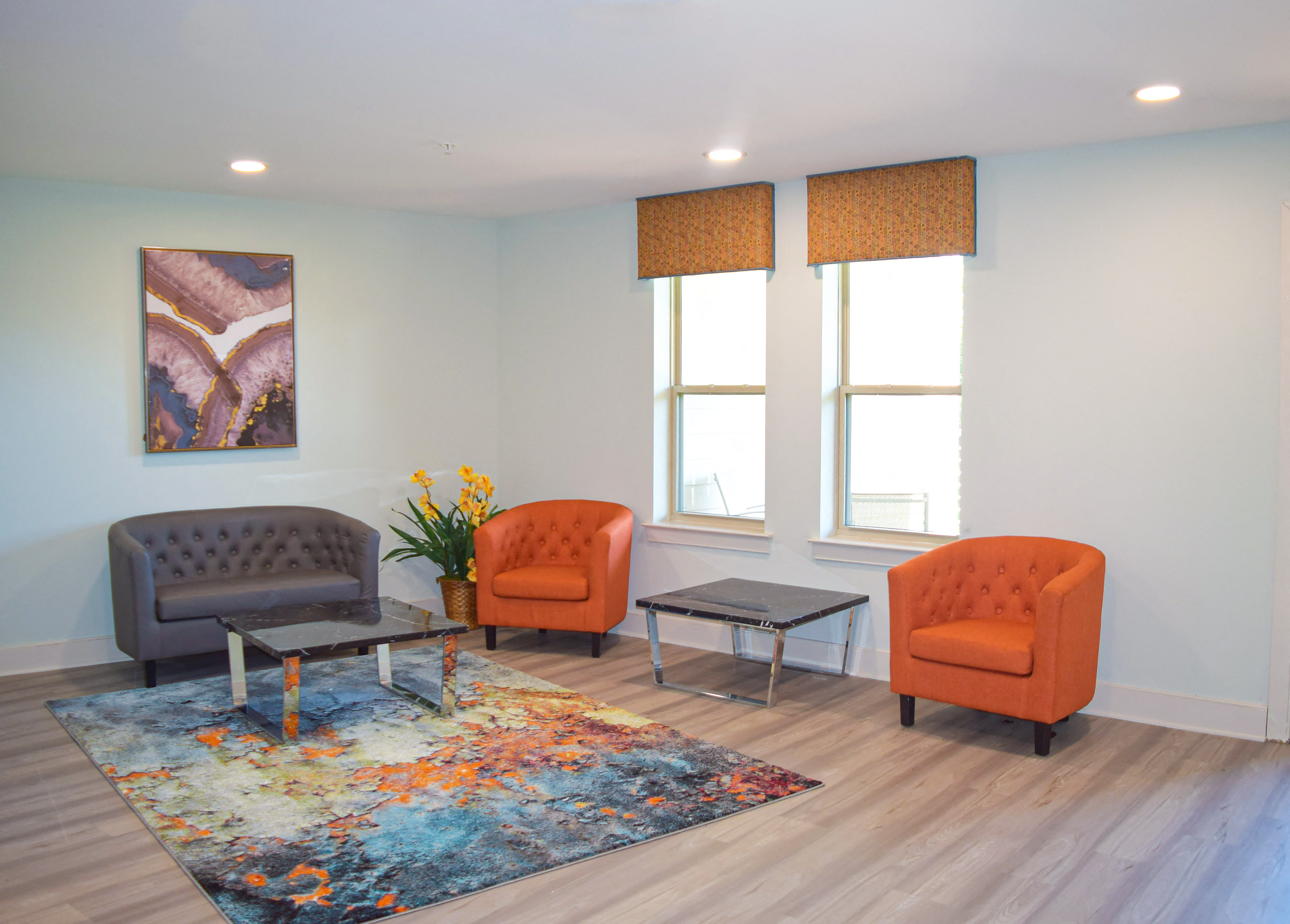 a living room with orange chairs and a blue rug and windows