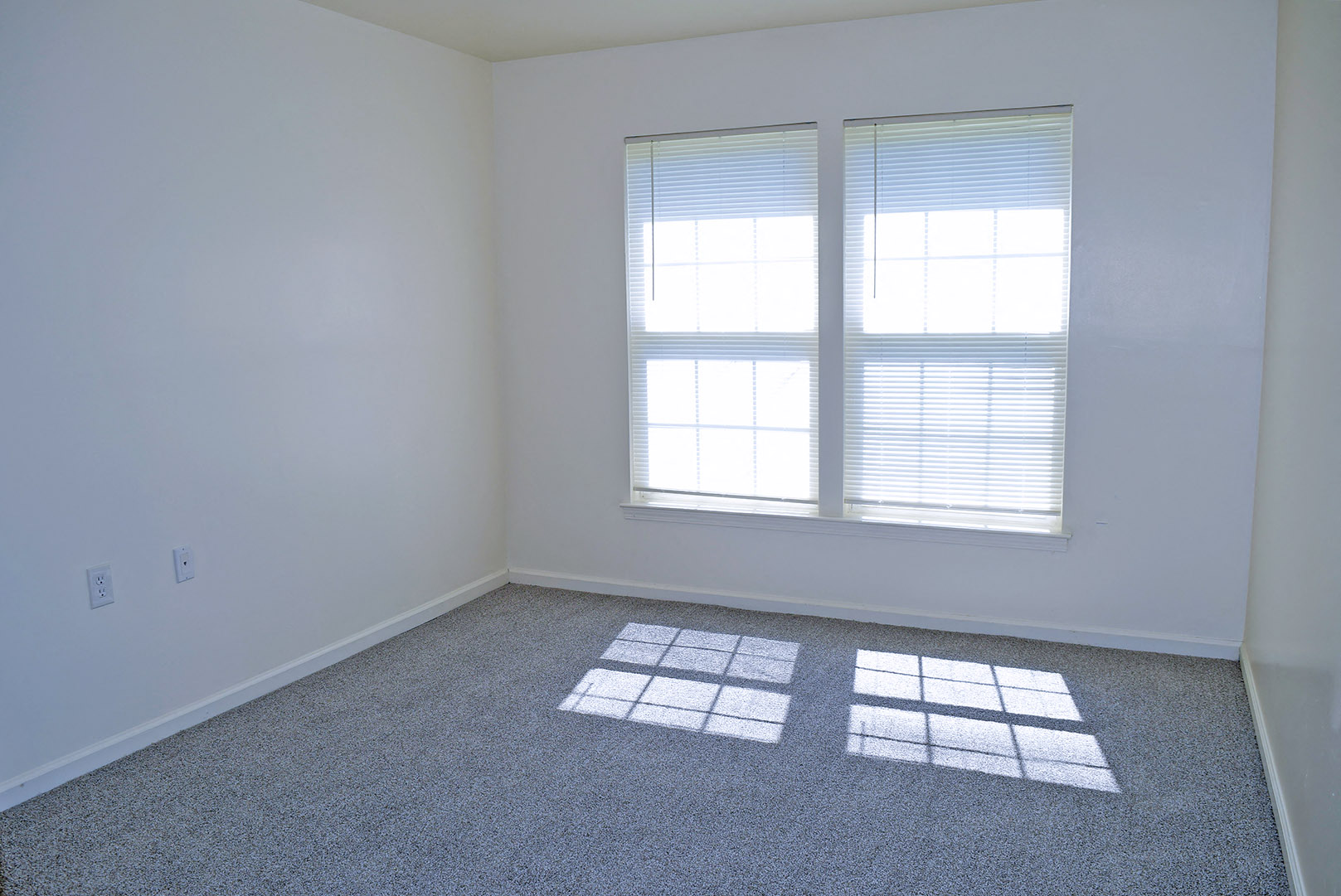 an empty room with two windows and a carpet