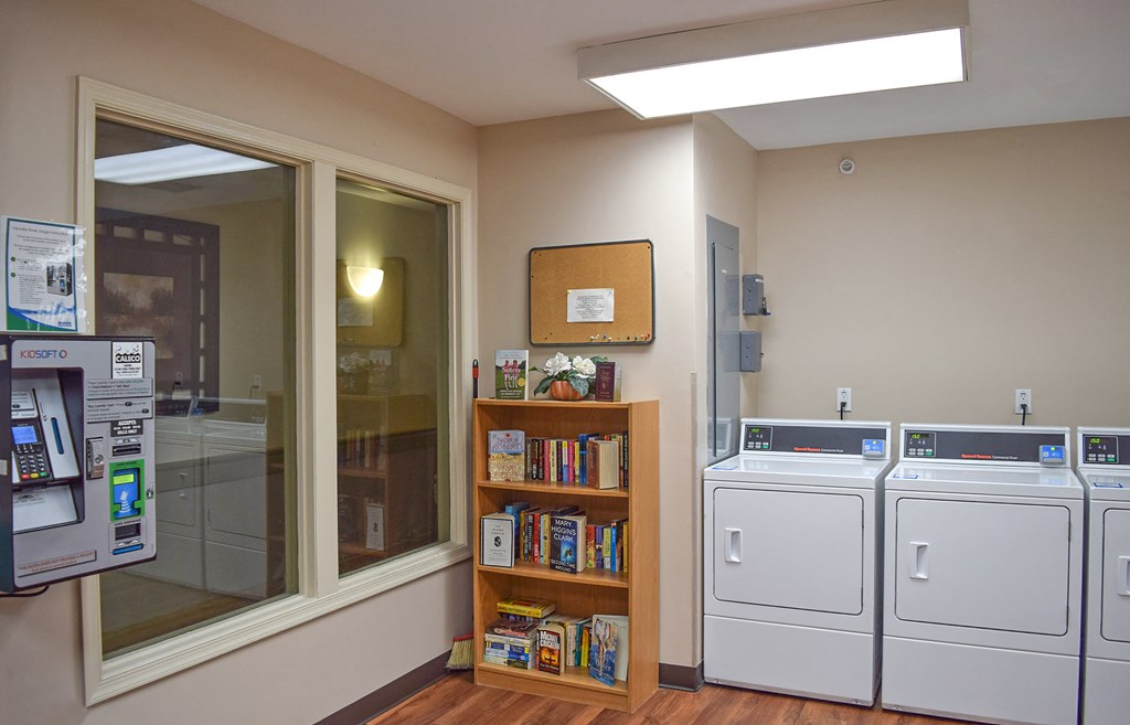 a laundry room with two washers and a window with a book shelf next to