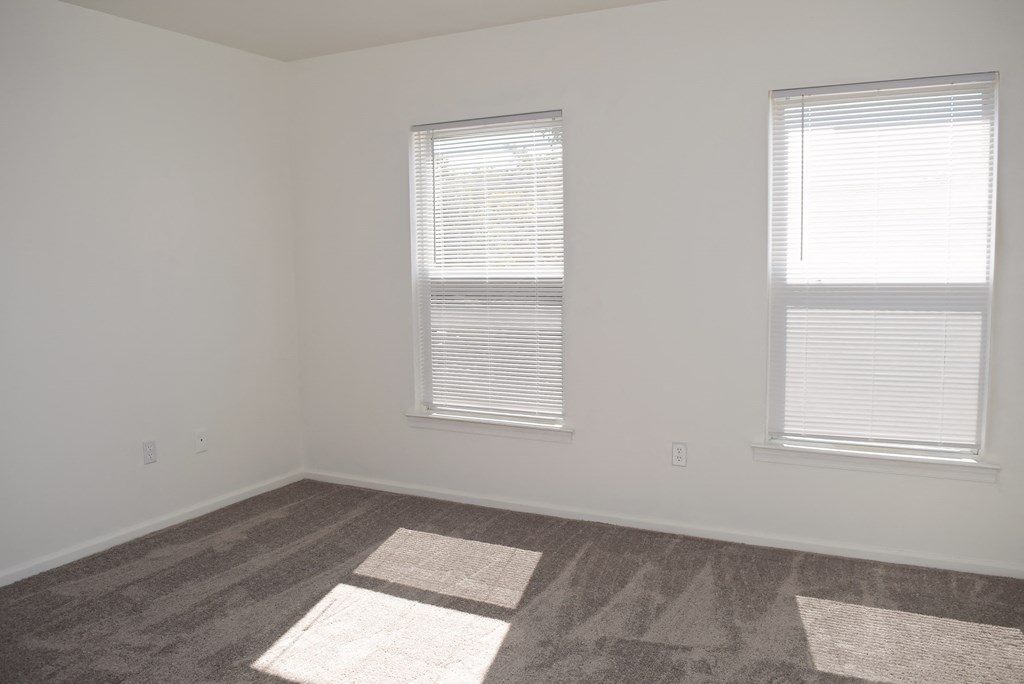 an empty room with two windows and a carpeted floor