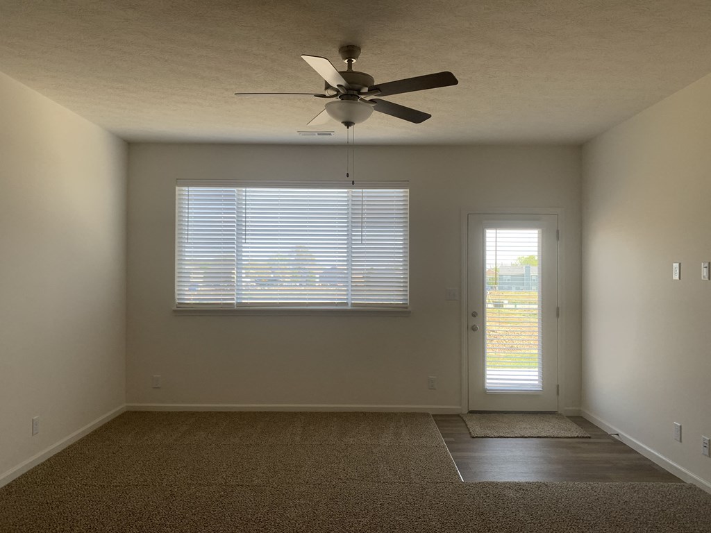 an empty living room with a ceiling fan and a window