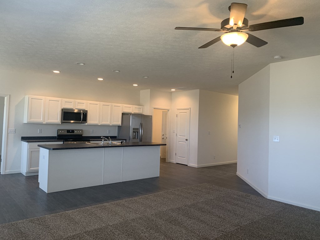 an empty living room and kitchen with a ceiling fan