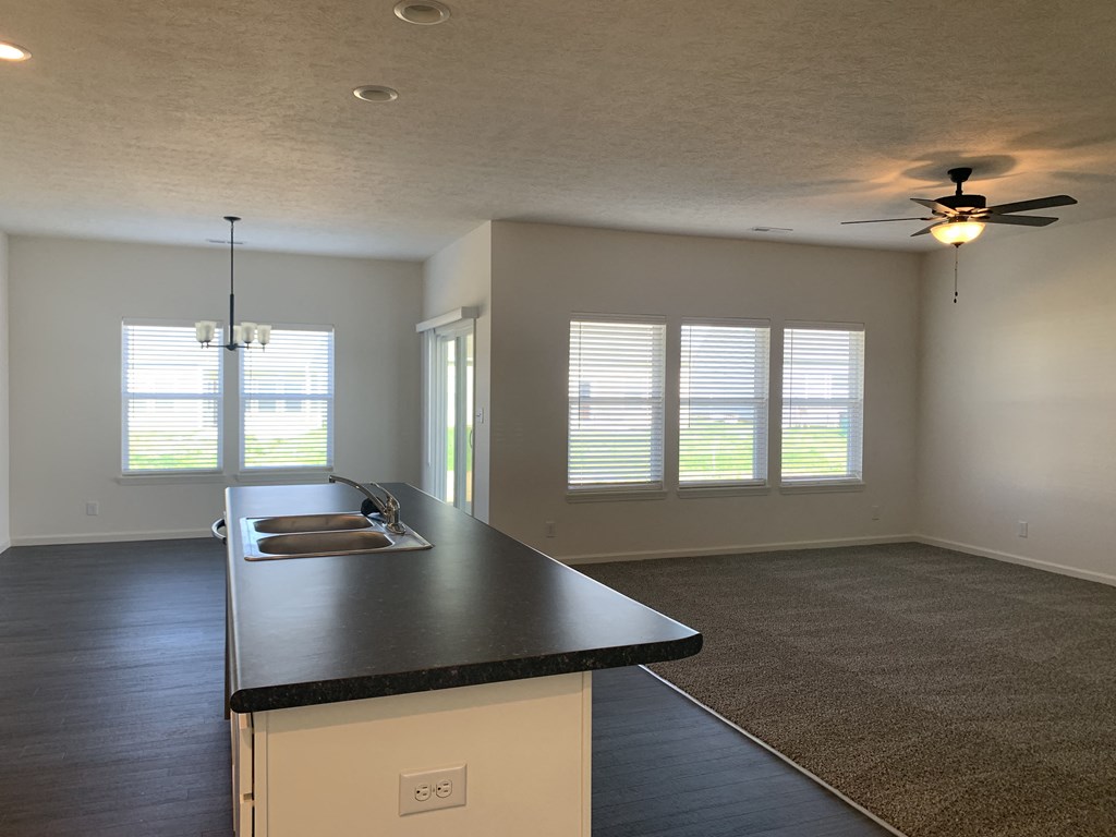 an empty living room with a kitchen and a ceiling fan