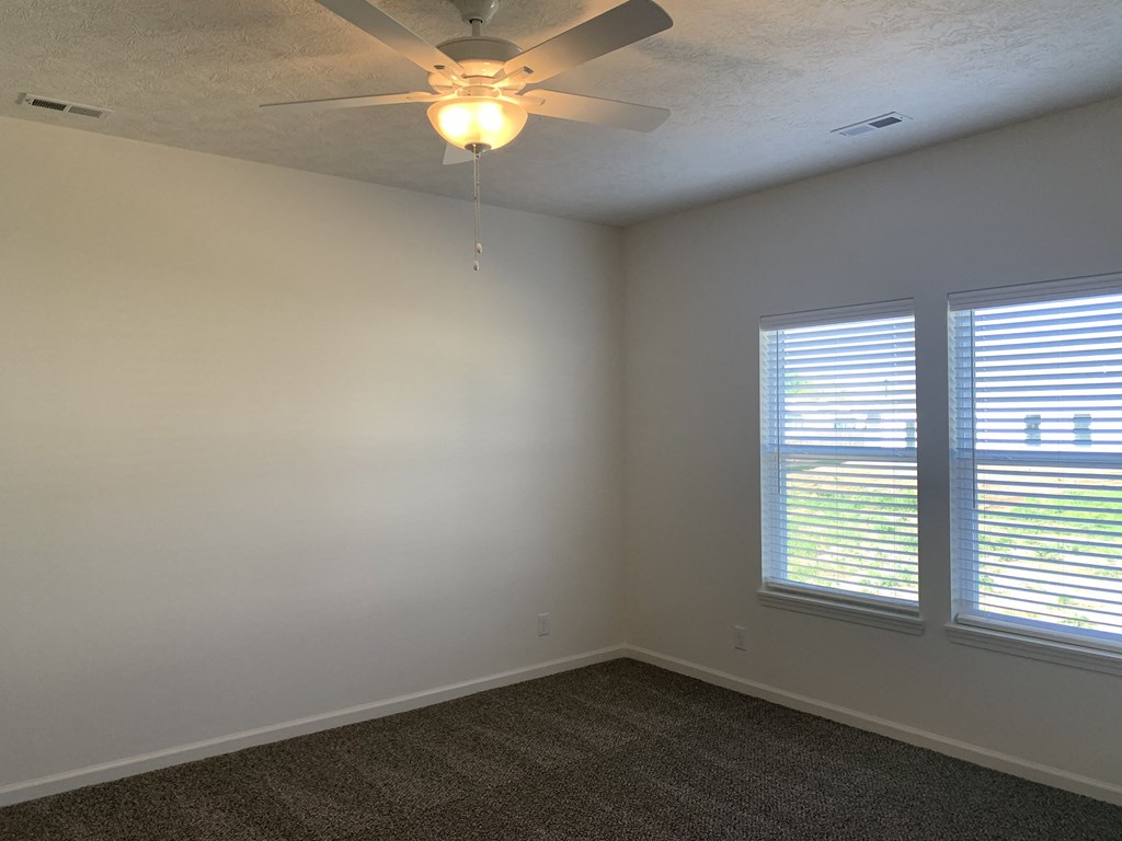 an empty room with a ceiling fan and two windows