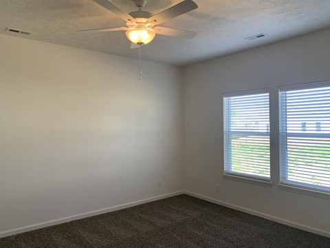 an empty room with a ceiling fan and two windows
